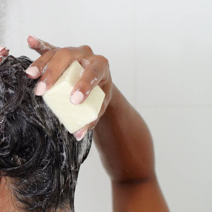 model uses Ethique shampoo bar to lather up hair in shower