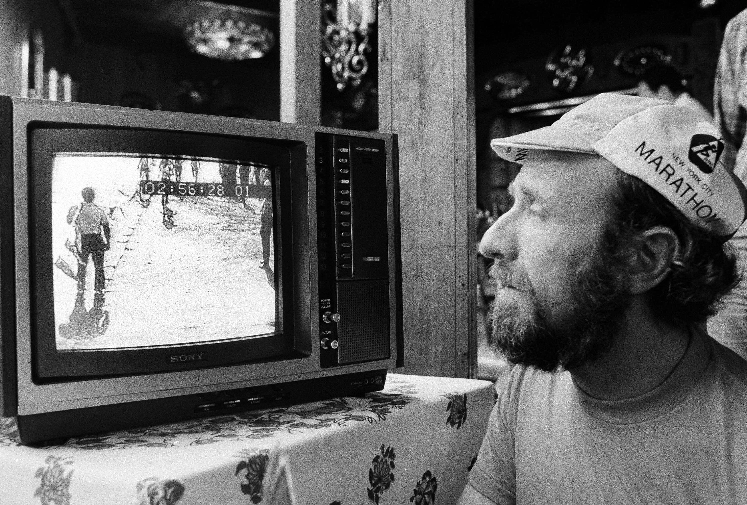 Man watches runners on a small TV