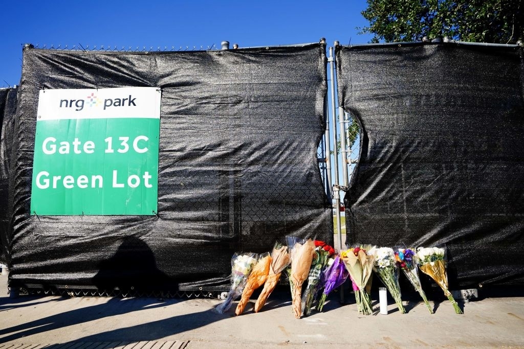 Bouquets of flowers placed on the ground against a gate outside NRG Park