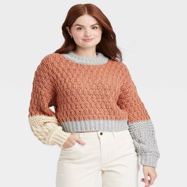 A model wearing a orange/cream/grey mock turtleneck sweater