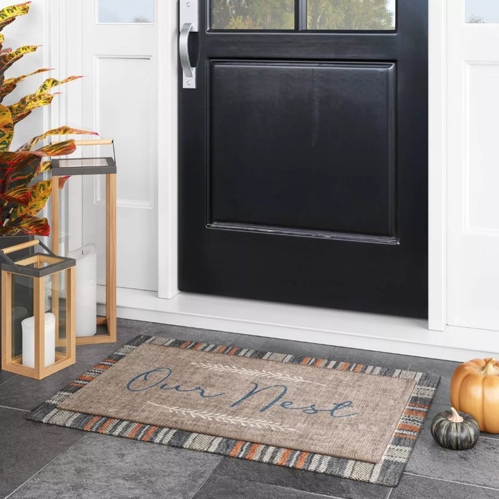 A doormat that reads "our nest" with fall leaf embroidery details