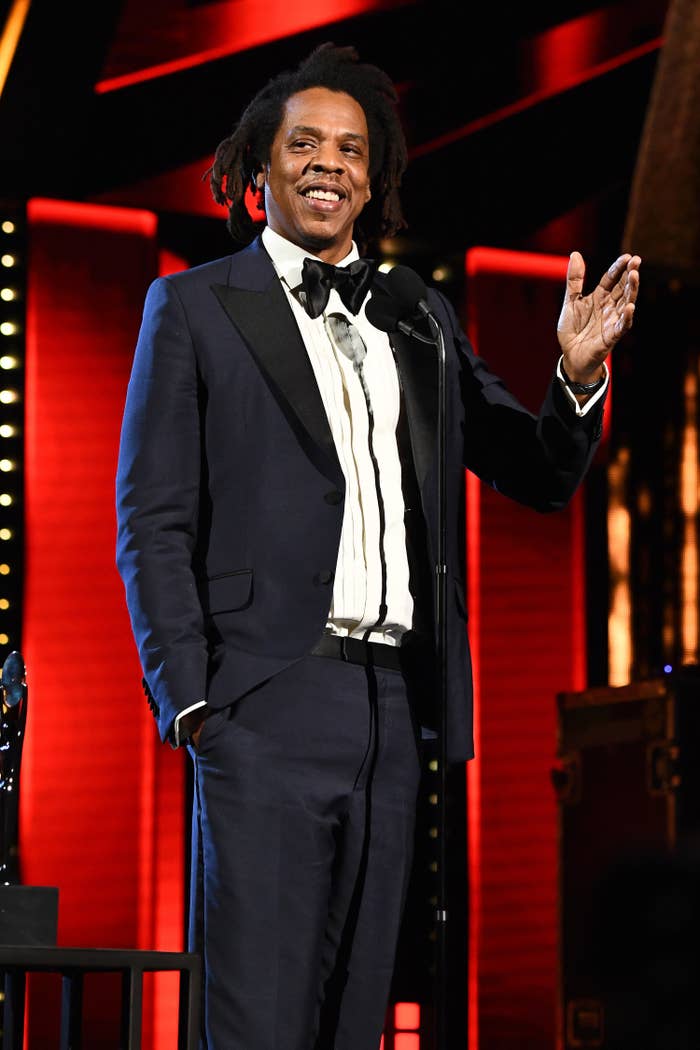 Jay-Z speaks in front of a microphone with his hand up