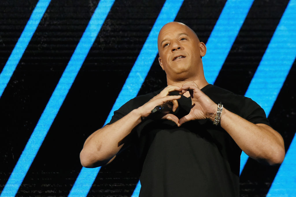 Vin Diesel speaks onstage and makes a heart gesture with his hands