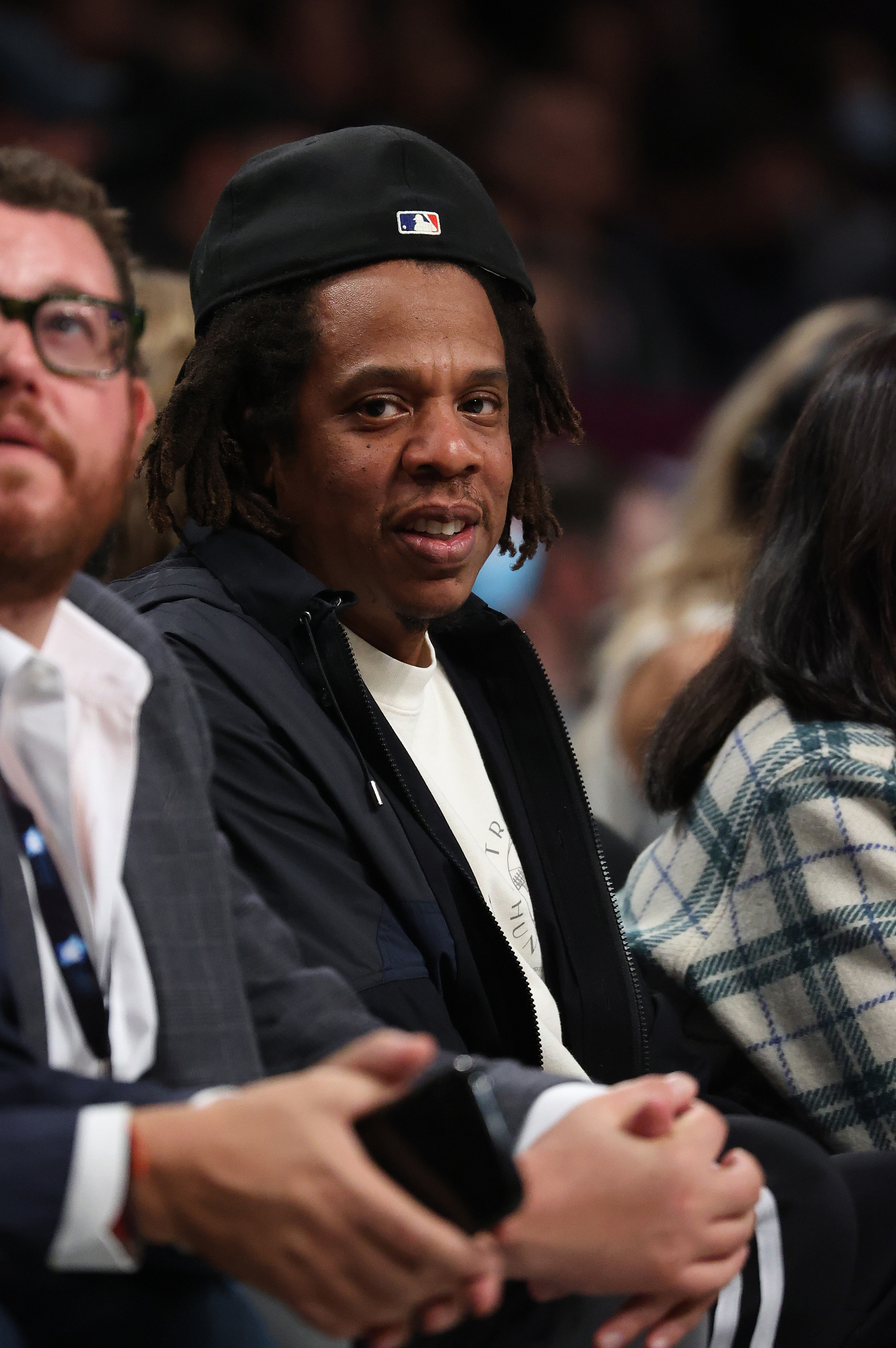 Jay-Z looks in the camera&#x27;s direction while sitting courtside at a basketball game