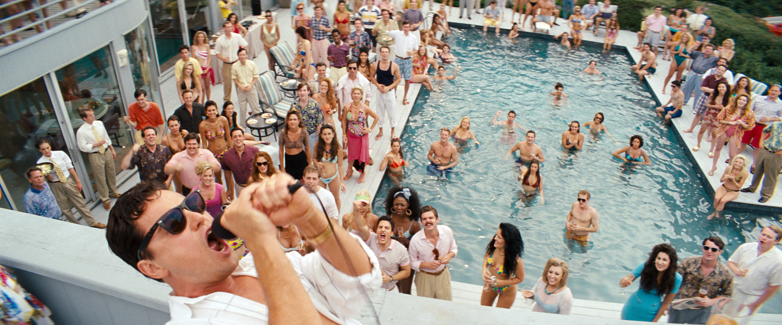 Jordan Belfort yells into a microphone at a luxurious pool party