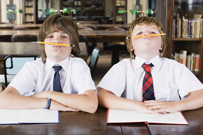 Two young school boys balancing pencils on their upper lips