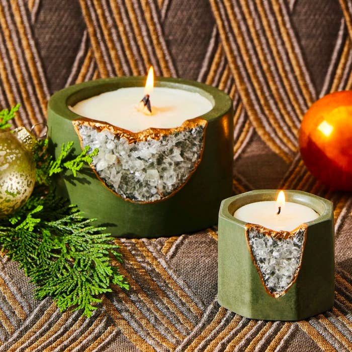 two candles in a geode vessels that have a deep evergreen shade plus gold leaf trim and crystal openings for the geode. the candles are small and large and both are lit.