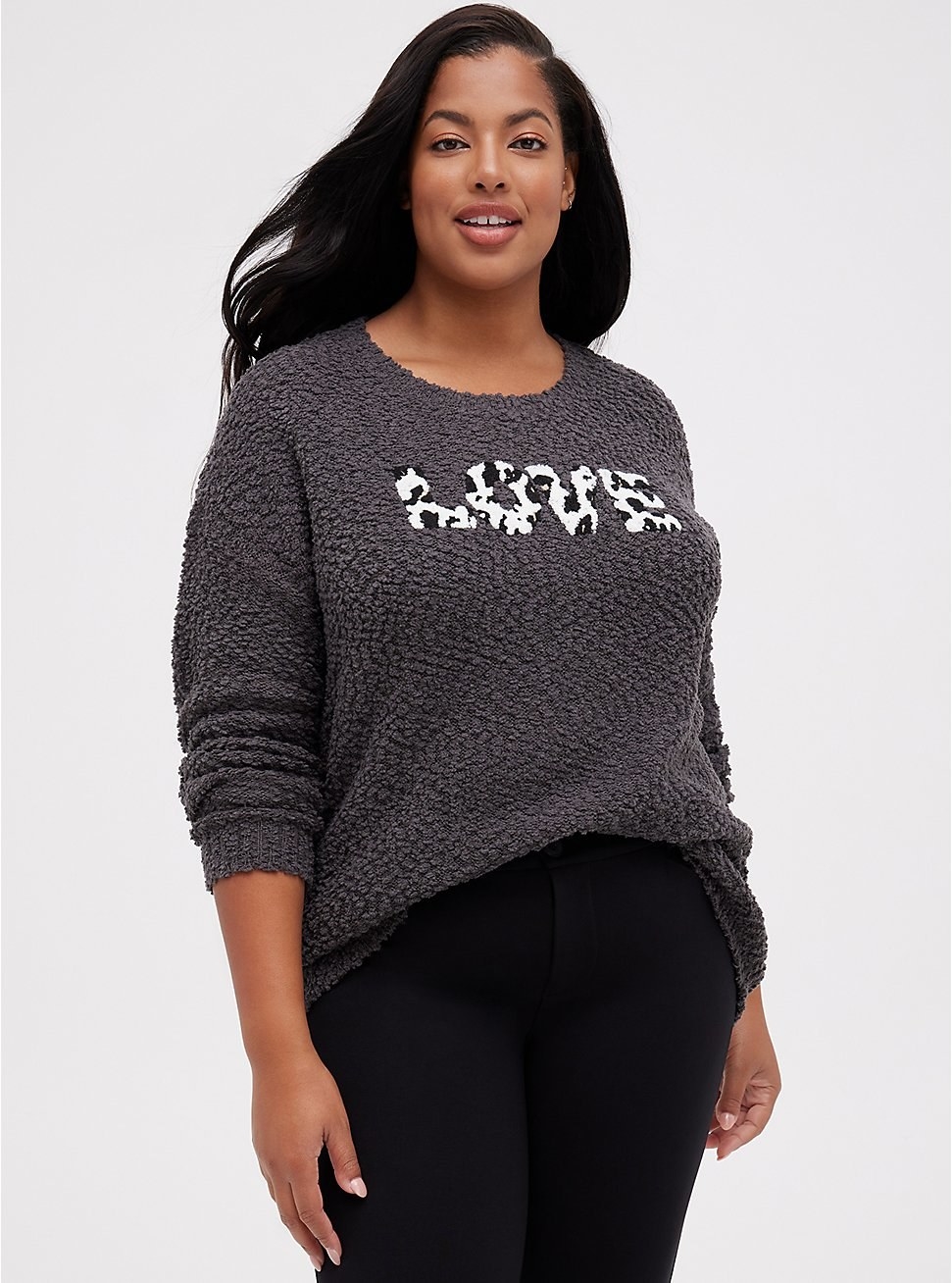 A model wearing the gray Love sweater slightly tucked into a pair of black jeans
