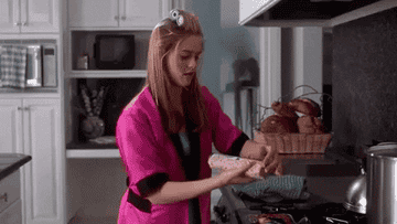 a gif of cher from clueless dropping a roll of cookie dough into the oven