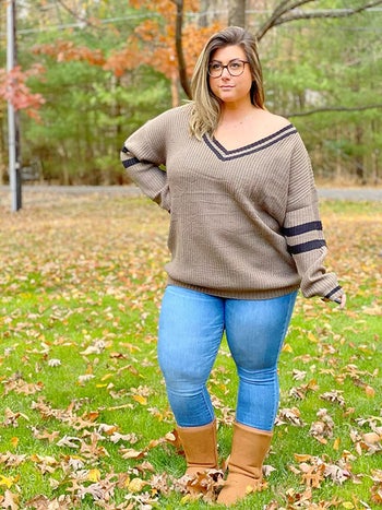 A reviewer poses outside wearing the sweater in khaki with blue jeans and brown boots