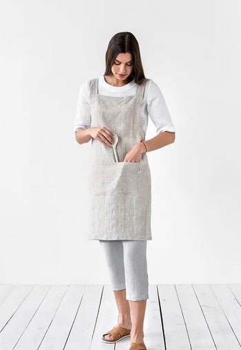 Model wearing the gray apron and placing a wooden spoon in the pocket