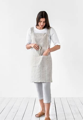 Model wearing the gray apron and placing a wooden spoon in the pocket