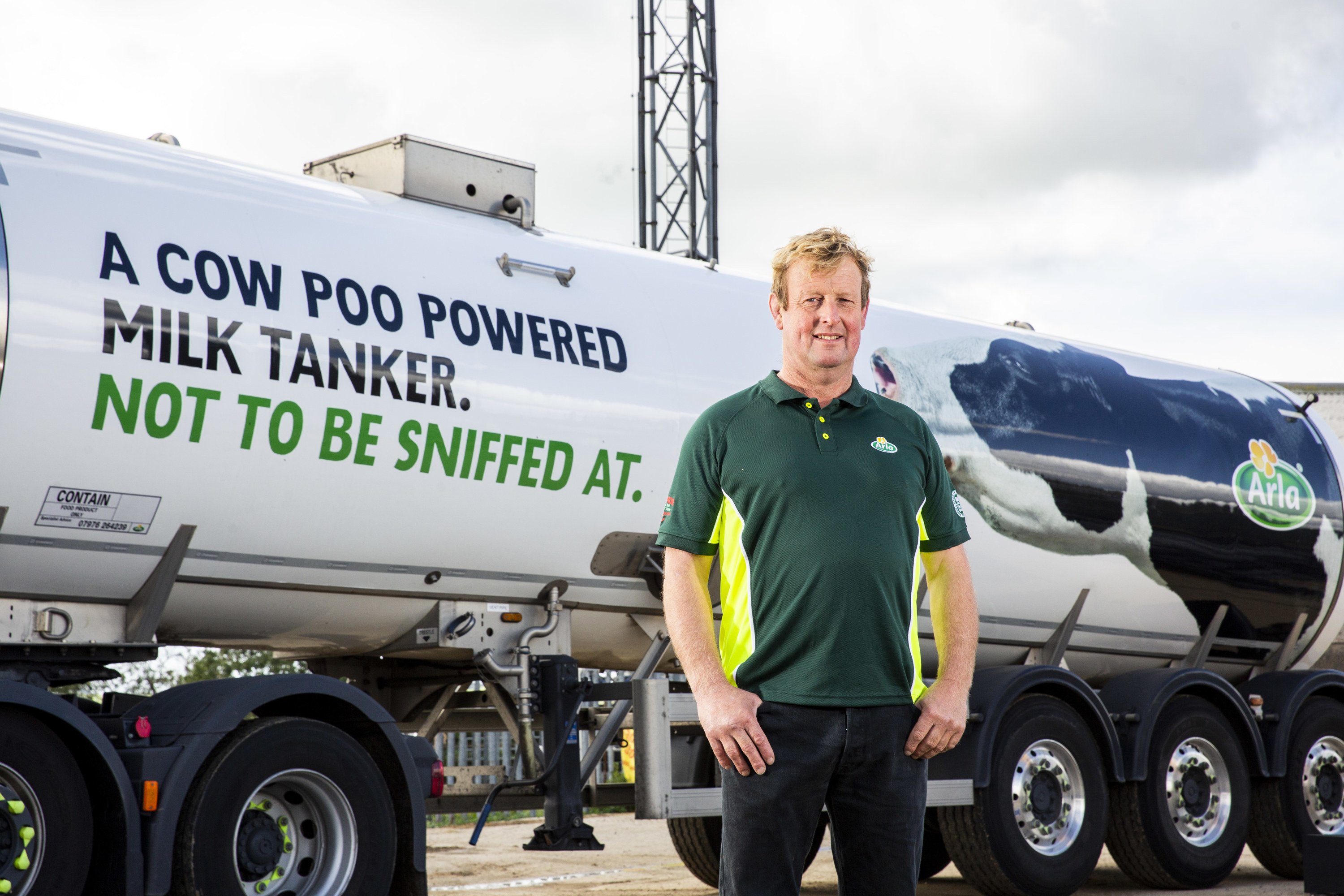 A male farmer stands infront of a milk tanker which says &quot;a cow powered milk tanker. Not to be sniffed at.&quot; on its side.