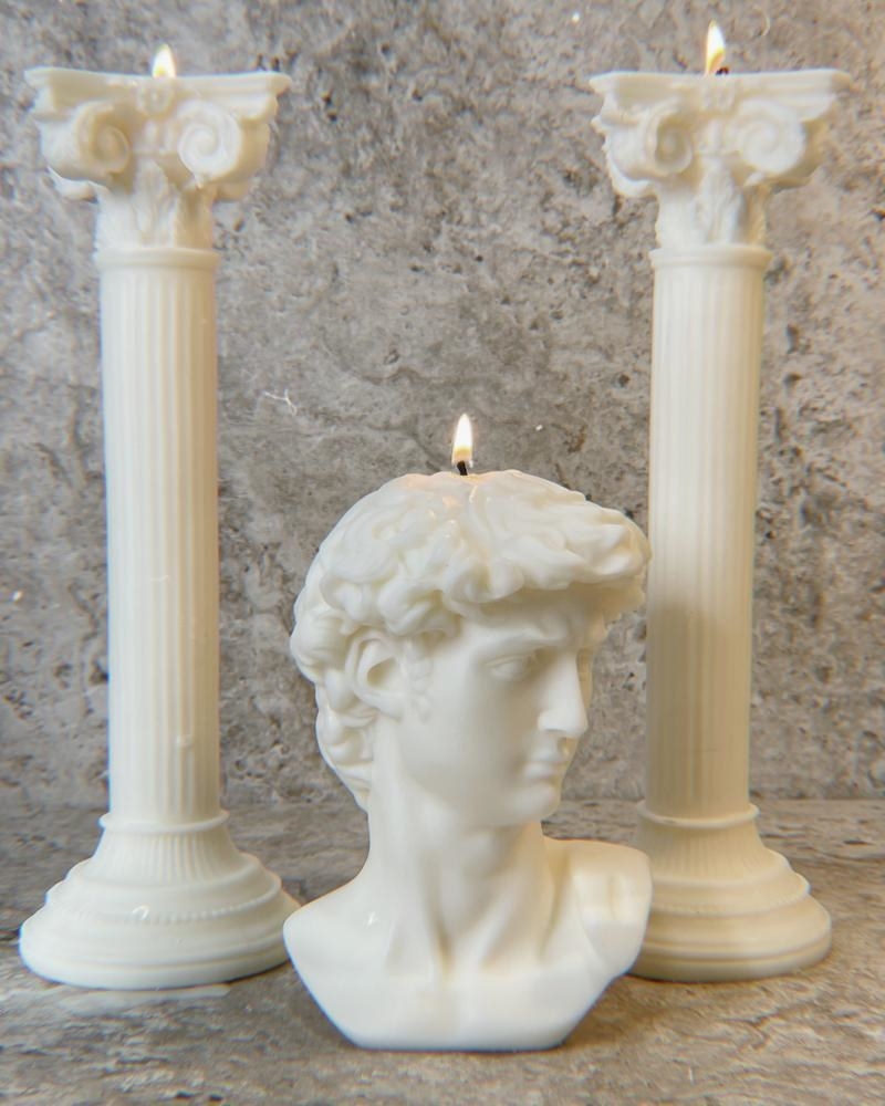 two candles shaped like ornate roman columns and a roman statue of a head