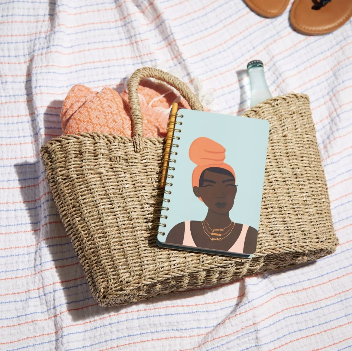 The journal has a light blue background and an illustration of an adult with dark skin, a coral hair wrap with, three layered gold-colored necklaces and a light pink top