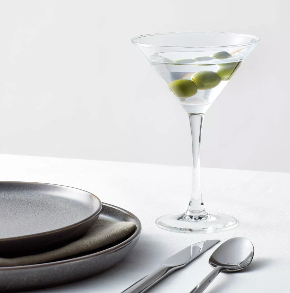 The clear martini glass is 3/4 of the way filled with a clear liquid and three green olives