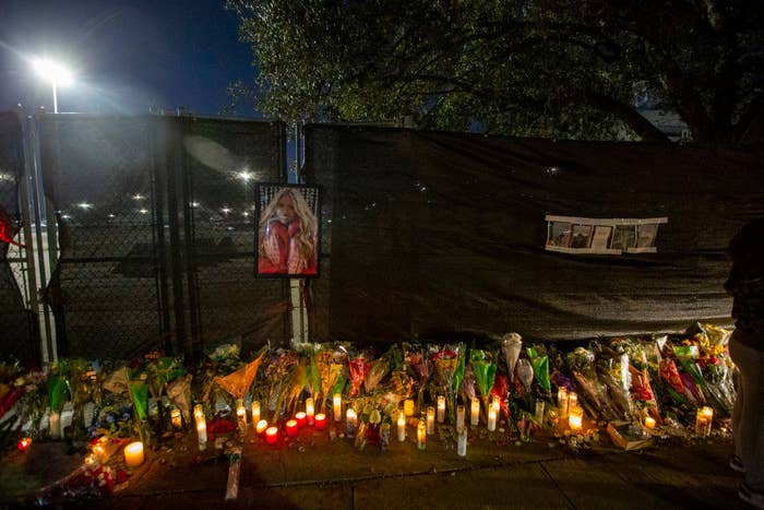 A memorial with candles, flowers, and photos at a fence