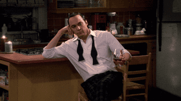 Sheldon sitting in a tuxedo holding a drink in his hand.