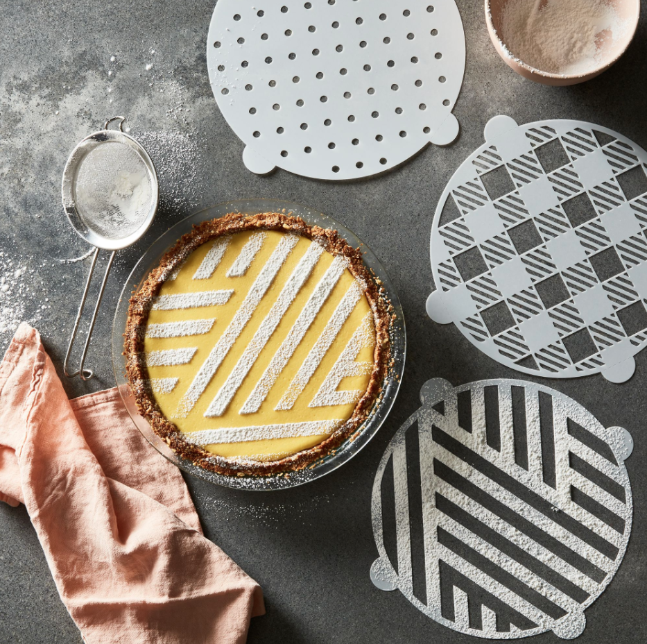 A pie that&#x27;s been decorated using one of the pie stencils, surrounded by three of the stencils