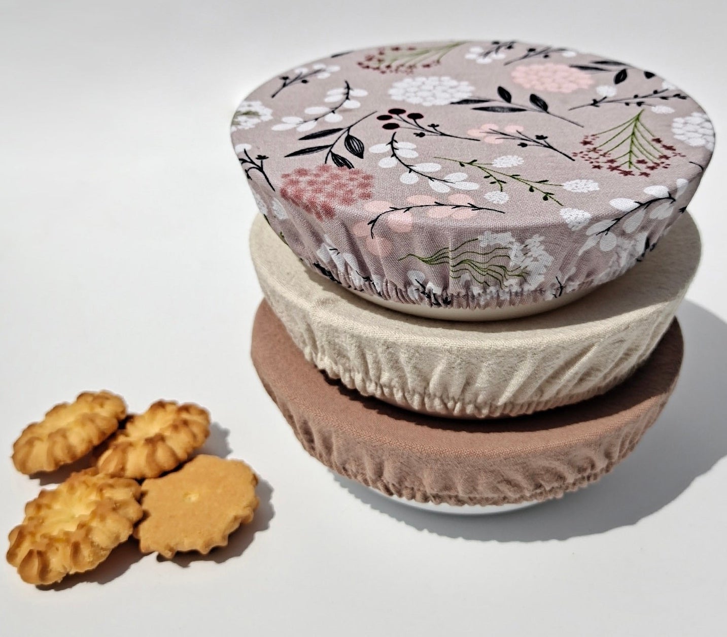 Three stacked bowls covered with the reusable covers next to some cookies