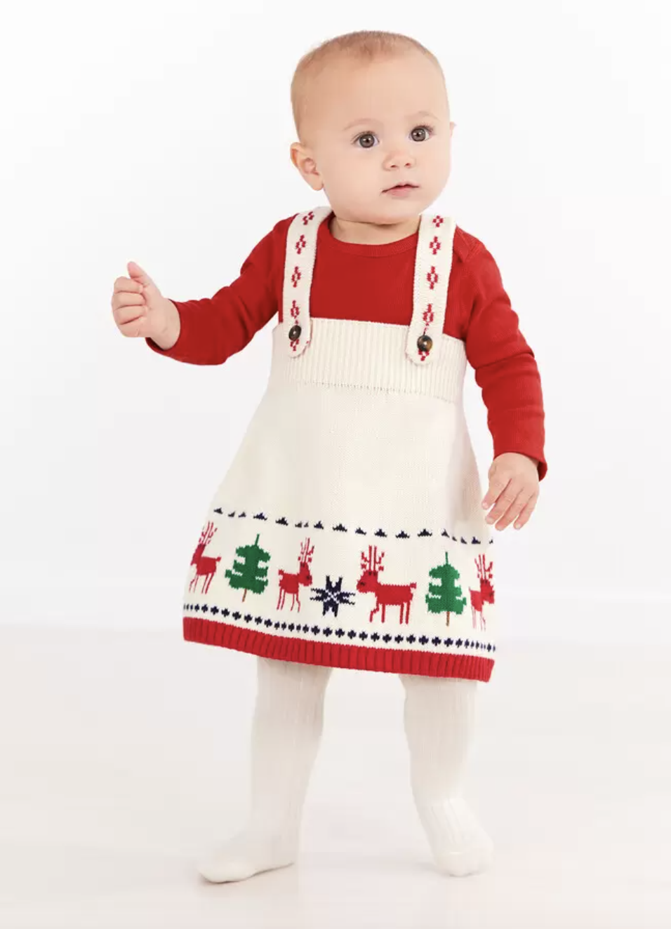 a baby in a white sweater jumper dress with holiday trees and deer on it