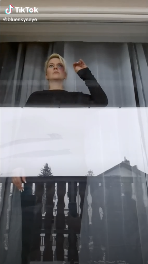 a woman stands at a window with her hands up