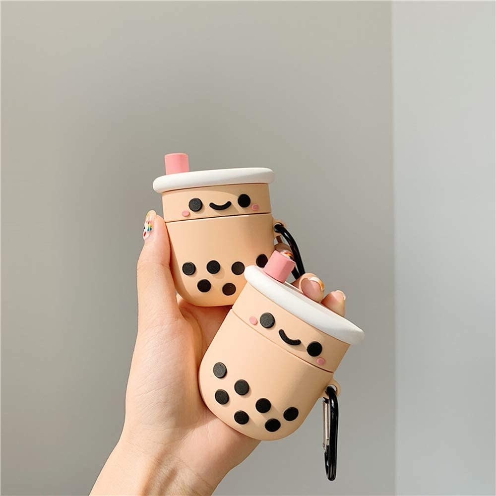 model holding two airpods cases shaped like smiling cartoon bubble tea cups with straws