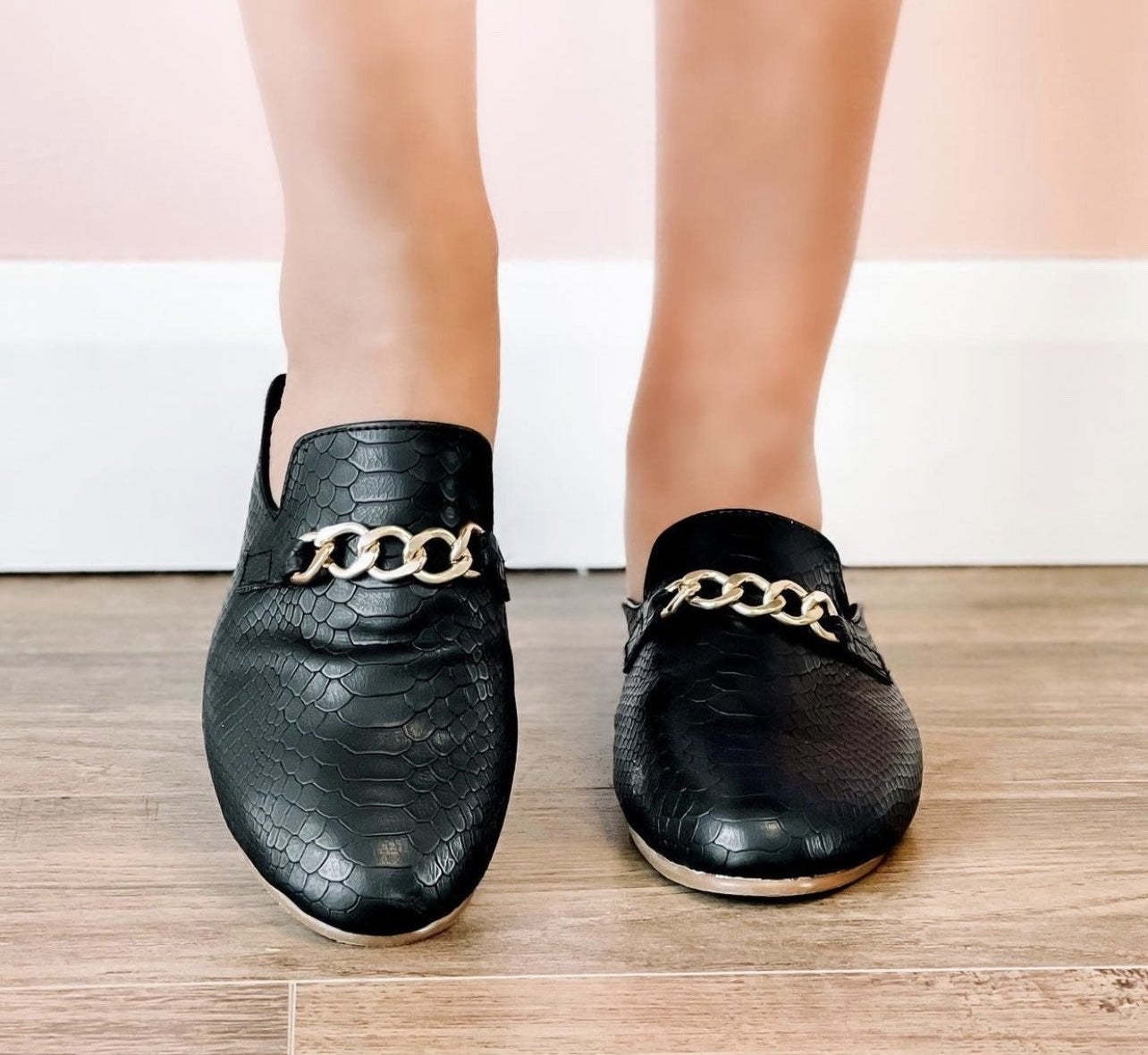 Model is wearing black vegan leather loafers with a gold chain buckle on the top