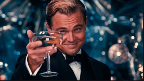 Leo holding out a glass of champagne as Jay Gatsby