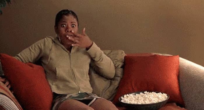 A woman eating popcorn on her couch while she watches a movie