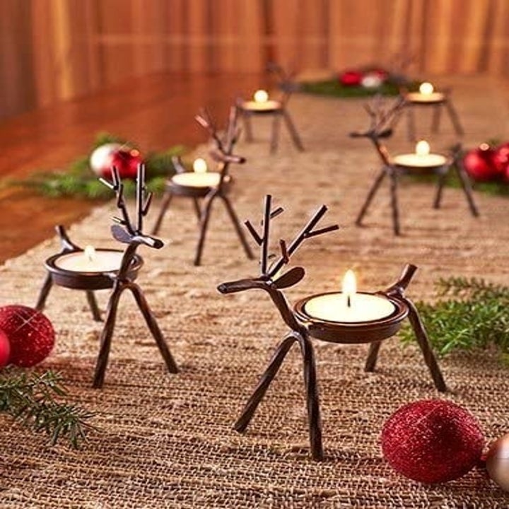 Several reindeer tea light holders arranged on a table runner next to other Christmas decor