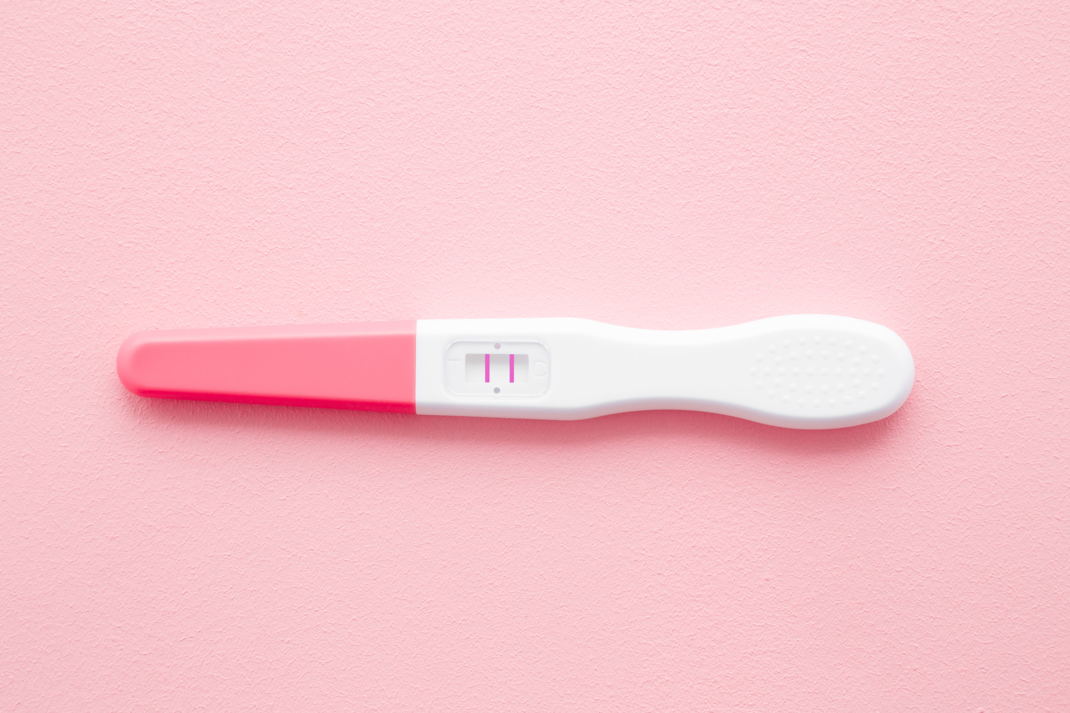 Pregnancy test with two stripes on pastel pink background