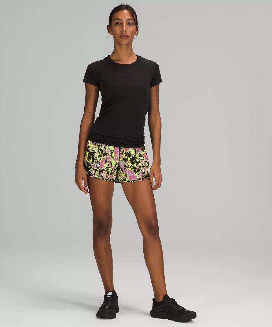 Model wearing neon yellow, black and pink patterned running shorts with black tee
