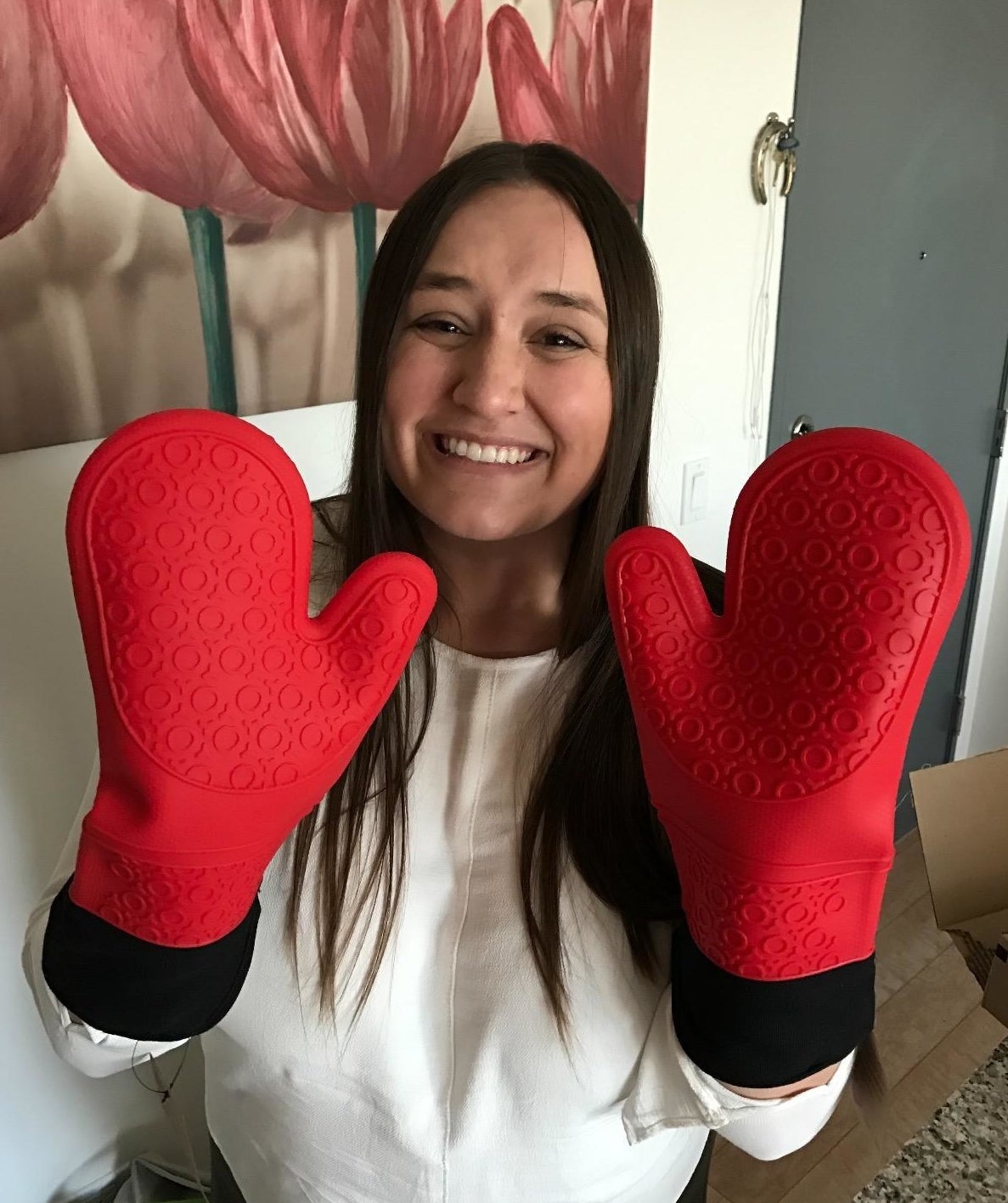 Smiling person holding up hands wearing large red silicone oven mitts
