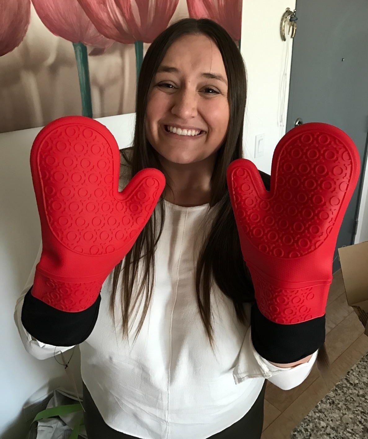 Smiling person holding up hands wearing large red silicone oven mitts