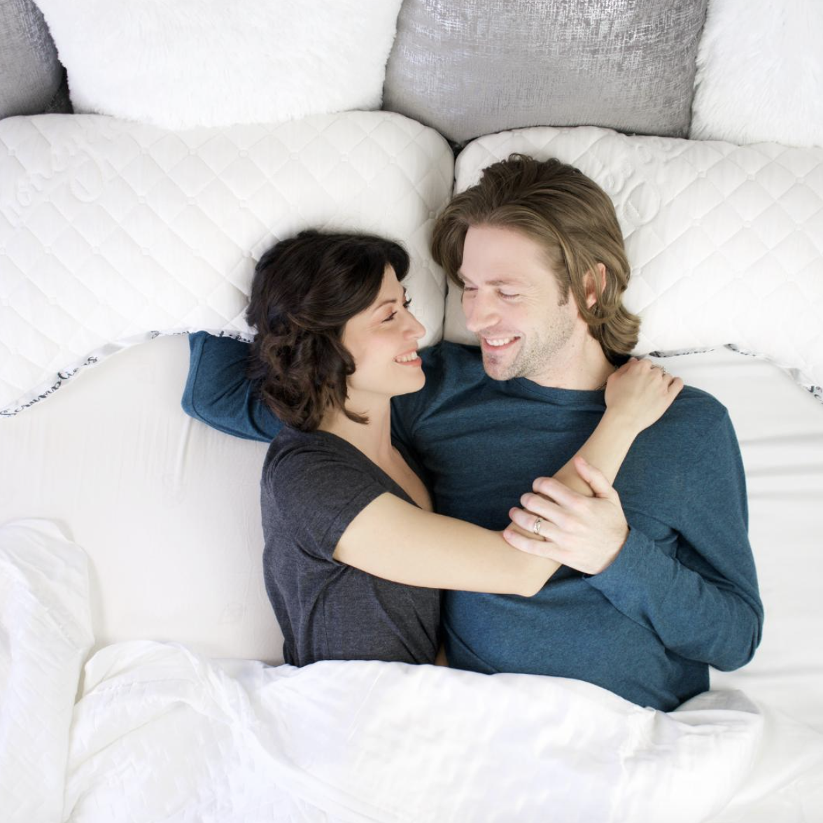a couple in bed. both are using curved pillows.