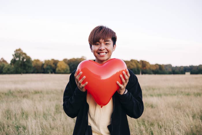 Young boy standing in a field holding a balloon heart.