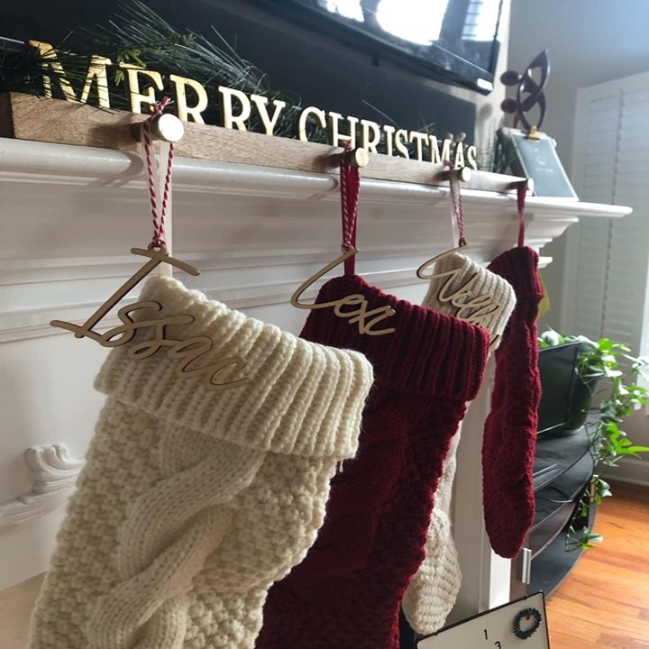 A different reviewer's mantle, which has four red and white stockings hanging from it attached to a wooden board with hooks on it. They've attached wooden name tags from Etsy as well.
