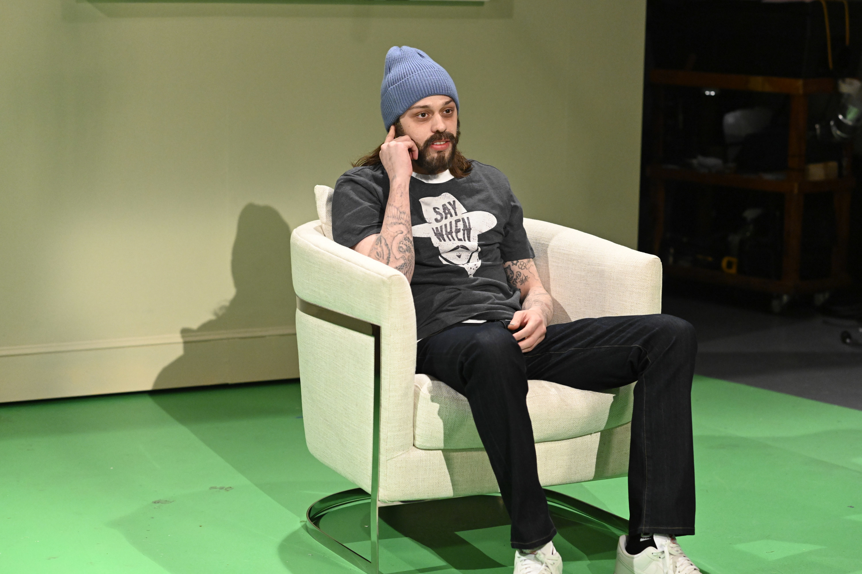 Pete as Aaron sitting on a couch wearing a beanie and a t shirt