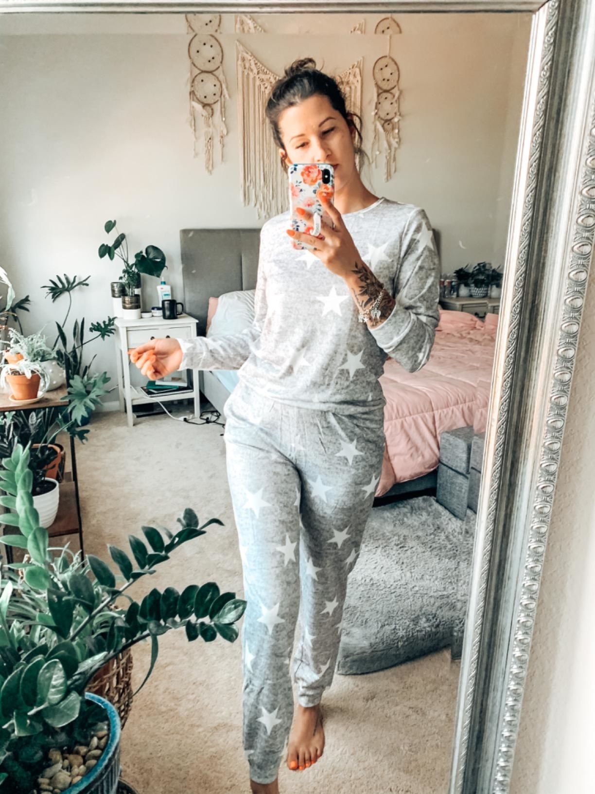 Reviewer is wearing a light grey long sleeve loungewear set with pants and white stars all throughout