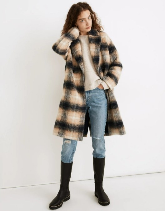 model wearing the plaid black and yellowish coat over a pair of jeans, black boots, and a cream sweater