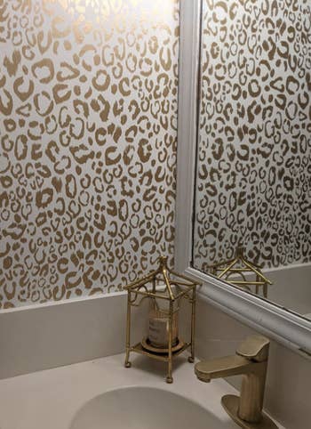bathroom corner with gold fixtures and decor that matches the wallpaper
