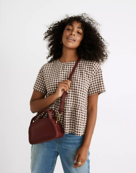 model wearing the burgundy crossbody with a brown and white gingham shirt and light blue jeans