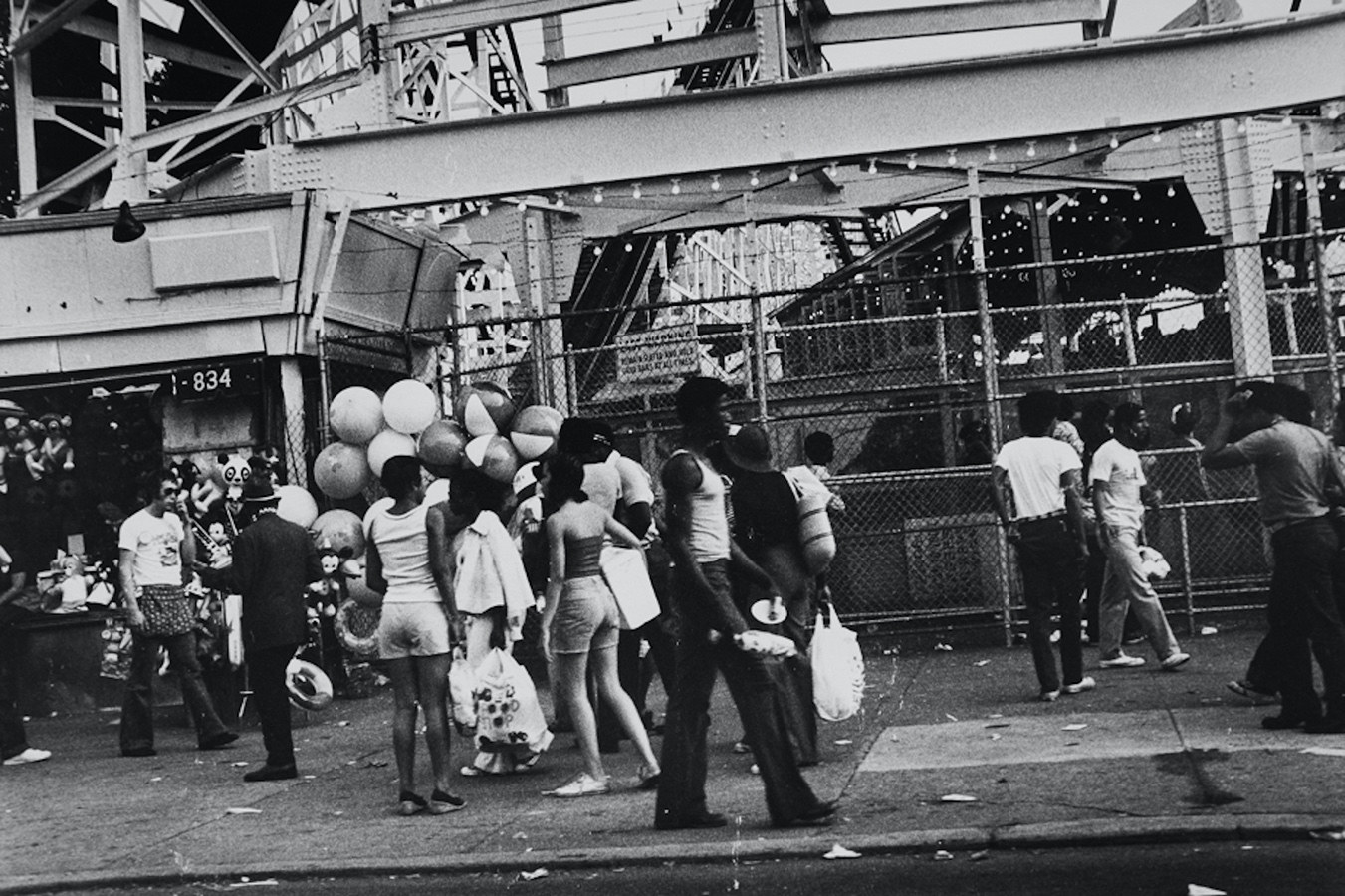 People walking on Coney Island, with big beach balls and a beach ball seller off to the side