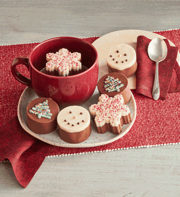 A gif of the cocoa bombs laid out on a holiday tray with someone mixing one into a cup
