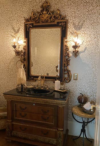 reviewer with grand gold mirror and the wallpaper behind it