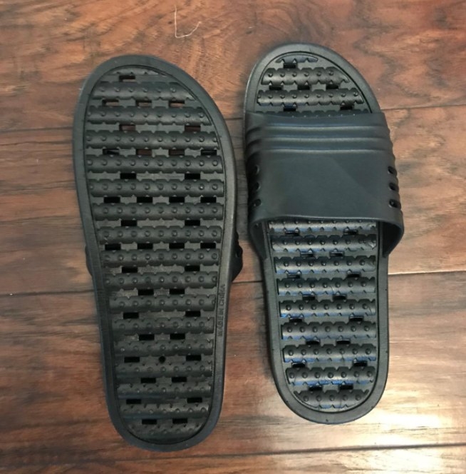 A pair of black shower shoes on reviewer&#x27;s wood floor