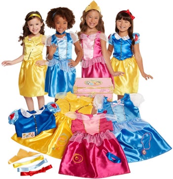 Four children dressed up as princesses standing next to a pink trunk and yellow, pink and blue satin costumes