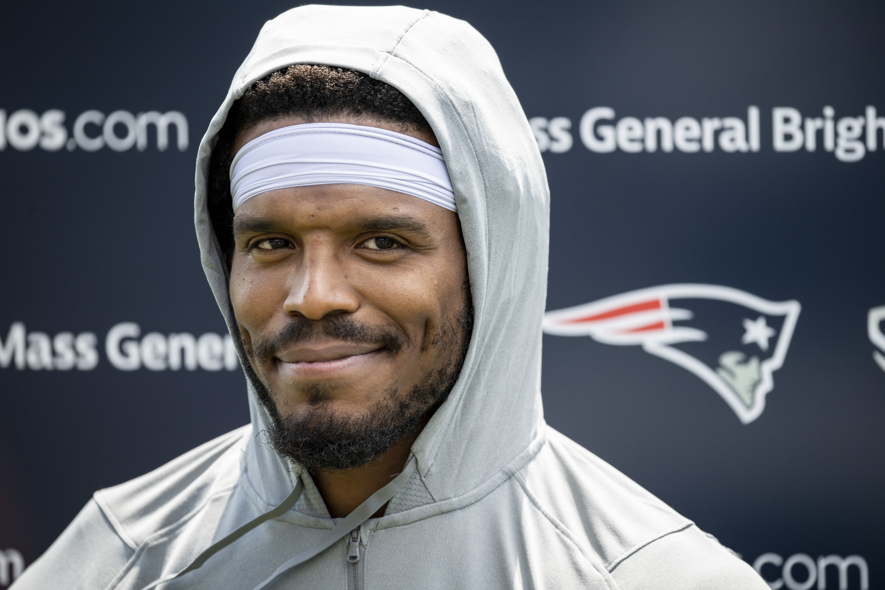 Cam Newton smiles in a gray hoodie at Patriots presser