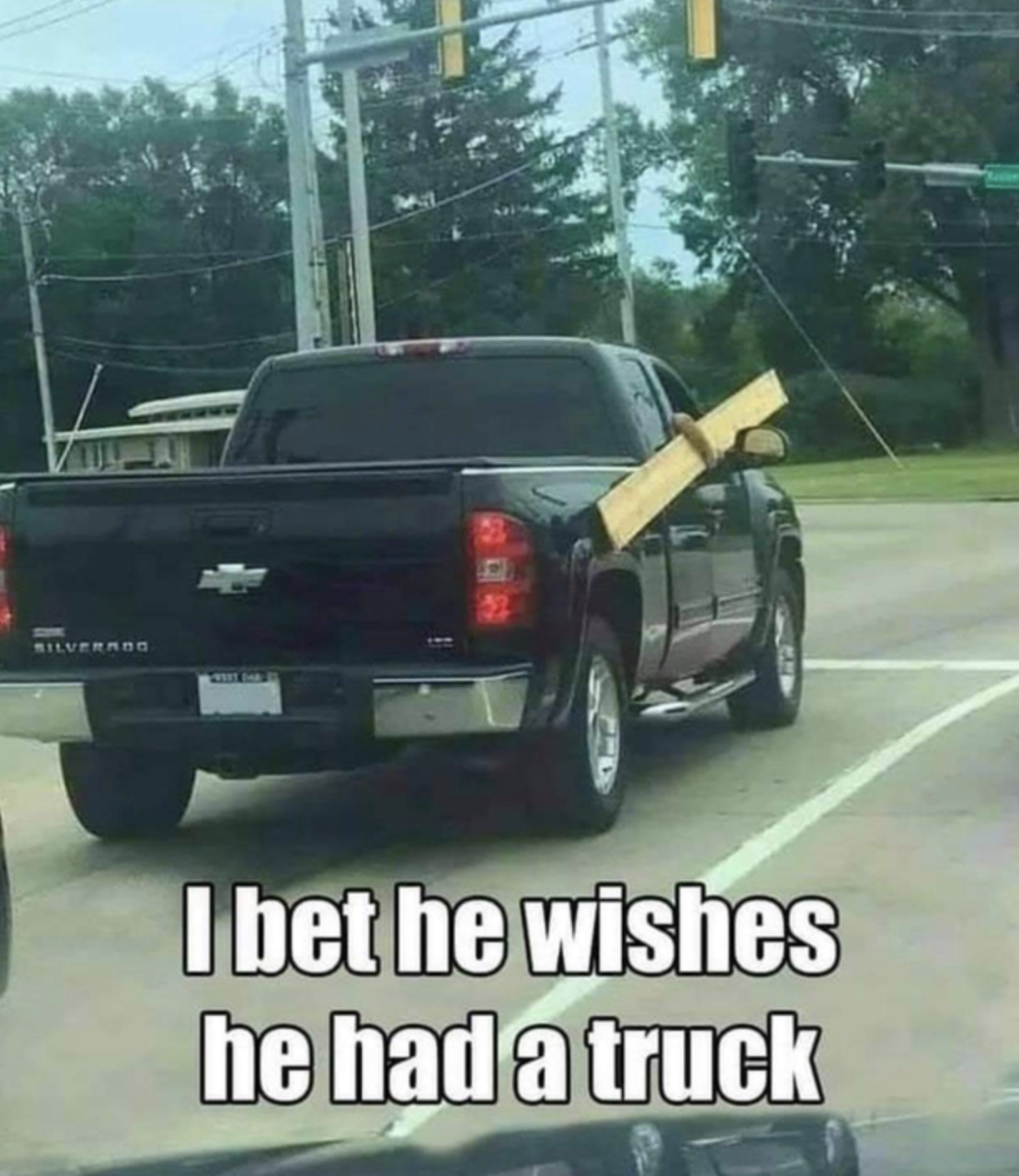 A pickup truck on the highway with a person in the passenger seat holding a plank of wood outside the car